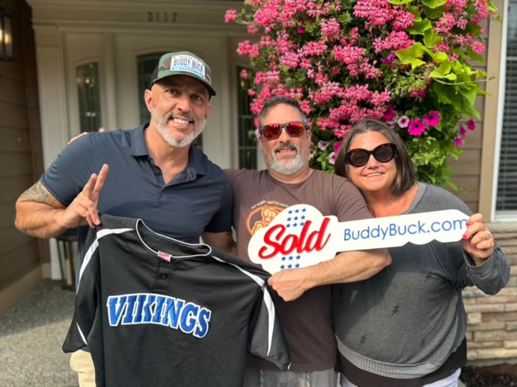 Buddy with Justin and Nicki at their new home in Tacoma, holding the BuddyBuck.com sign and a Curtis Vikings jersey